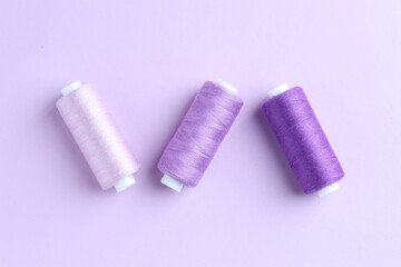 Spools of colorful sewing threads on lilac background, flat lay