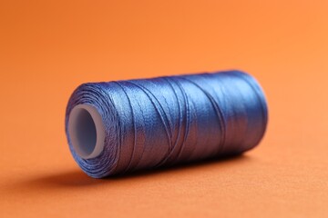 Spool of blue sewing thread on orange background, closeup