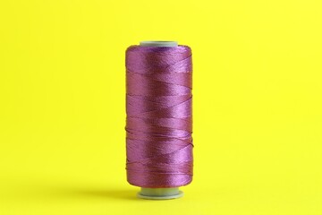 Spool of purple sewing thread on yellow background