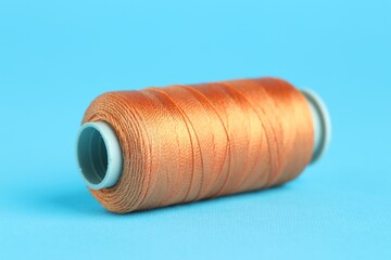 Spool of orange sewing thread on light blue background, closeup