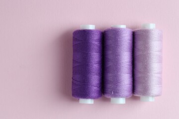 Spools of colorful sewing threads on pink background, flat lay. Space for text