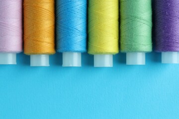 Spools of colorful sewing threads on light blue background, flat lay. Space for text