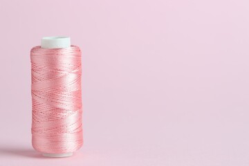 Spool of sewing thread on pink background, space for text