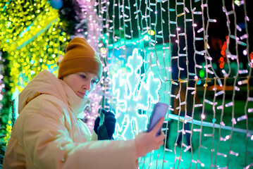 a girl takes a selfie in Christmas decorated with holiday lights. New Year's Eve, festive atmosphere