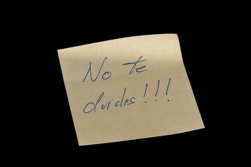Yellow adhesive paper, similar to a Post-it note, on a black background with the words “No te olvides” in Spanish handwritten in blue ink.