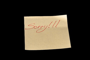 Yellow adhesive paper, similar to a Post-it note, on a black background with the word "Sorry" and three exclamation marks handwritten in red ink.