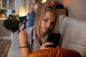 A teenager fully engaged with their smartphone while lounging comfortably in a cozy living space