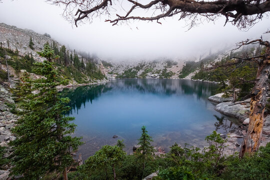 Misty alpine lake surrounded by rocky terrain and verdant forests
