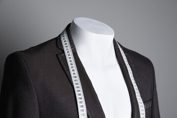 Semi-ready jacket with tailor's measuring tape on mannequin against grey background, closeup