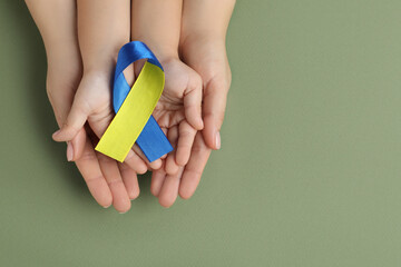 Woman with child holding yellow and blue ribbon on green background, top view. Down syndrome awareness