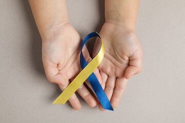 Child with yellow and blue ribbon on dark beige background, top view. Down syndrome awareness