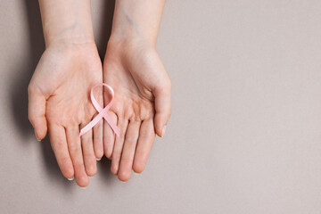 Woman with pink ribbon on grey background, top view and space for text. Breast cancer awareness