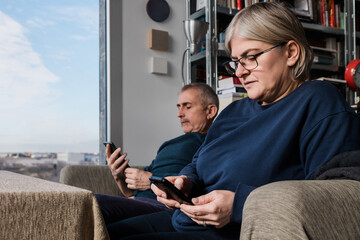 Senior couple comfortably using smartphones at home