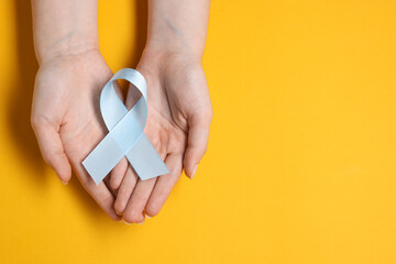 Woman with light blue ribbon on yellow background, top view and space for text. Childhood cancer awareness