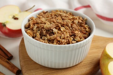 Delicious apple crisp in bowl, fresh fruits and cinnamon sticks on white table, closeup