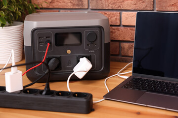 Laptop charging from portable power station on wooden desk indoors