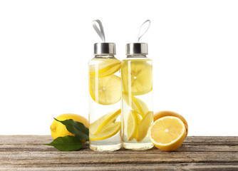 Lemon water in bottles and fresh fruits on wooden table against white background