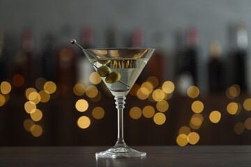 Martini cocktail with olives in glass on wooden table against blurred background. Bokeh effect