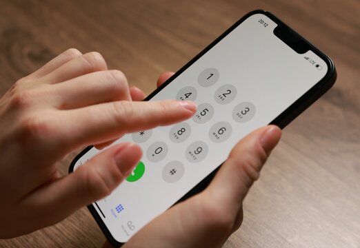 Woman dialing number on smartphone at wooden table, closeup