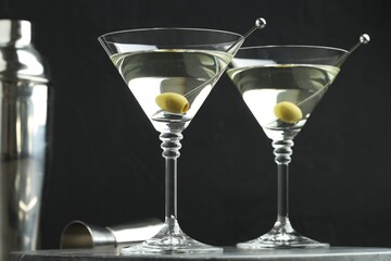 Martini cocktail with olives in glasses on grey table against black background, closeup