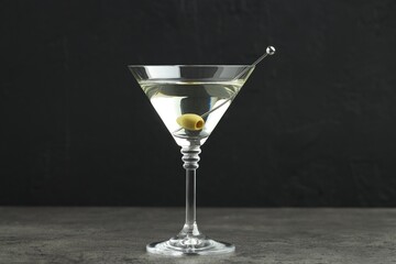Martini cocktail with olives in glass on grey table against black background