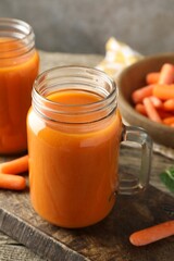 Fresh carrot juice in mason jars and vegetables on wooden table against gray background, closeup