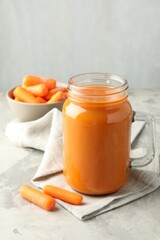 Fresh carrot juice in mason jar and vegetables on gray textured table