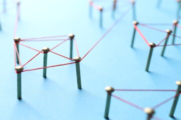 Network connection. Nails linked together by thread on light blue background, closeup