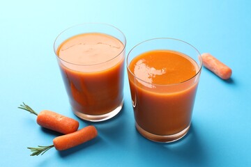 Fresh carrot smoothie in glasses and vegetables on light blue background, closeup