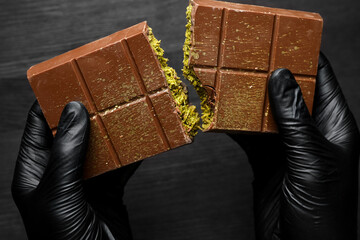 Woman breaking Dubai chocolate bar with pistachio and knafeh at dark table, closeup