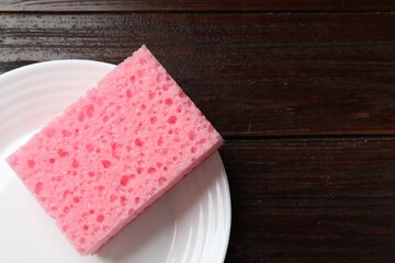 Pink sponge and plate on wooden table, top view. Space for text