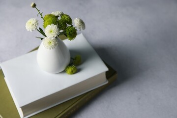 Books and vase with beautiful flowers on grey table, closeup. Space for text