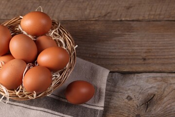Wicker basket with fresh eggs on wooden table, top view. Space for text