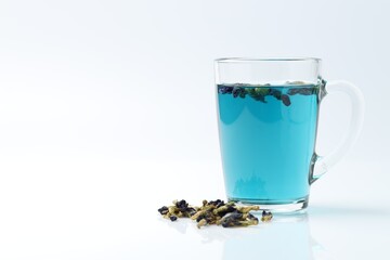 Fresh butterfly pea flower tea in cup and dry petals on white table, closeup. Space for text
