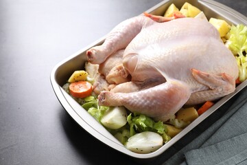 Raw turkey and vegetables in baking dish on grey table, closeup