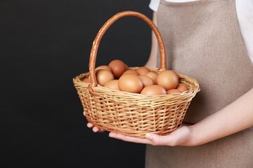 Woman with basket of eggs on black background, closeup. Space for text