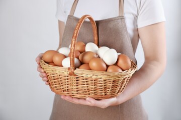 Woman with basket of eggs on light background, closeup