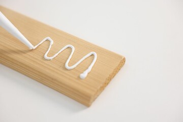 Glueing wooden plank with caulking gun at white table, closeup