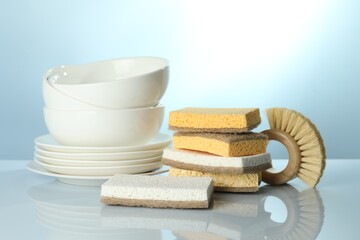 Stack of sponges, brush and dishware on light table, closeup