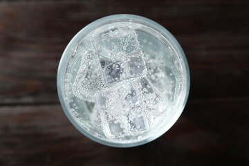 Refreshing soda water with ice cubes in glass on wooden table, top view