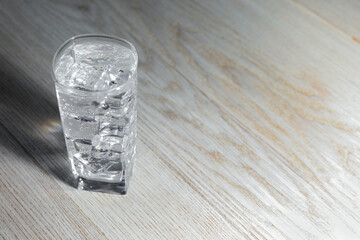 Refreshing soda water with ice cubes in glass on light wooden table, closeup. Space for text