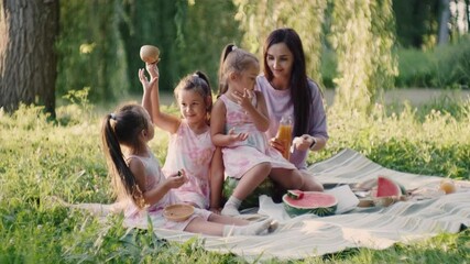 Young parents with  pretty daughters spending free time at green garden and eating tasty watermelon. Happy family having summer picnic during weekends outdoors. Parents eating watermelon on picnic.