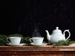 Fototapeta premium A rustic tea setup on a wooden table with a ceramic teapot, matching teacups, and festive pine sprigs, creating a cozy holiday atmosphere. Generative AI