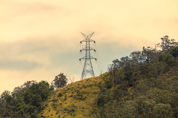 Photograph of a large electricity Transmission Tower on a grassy hill against an orange sunset sky in regional Australia.