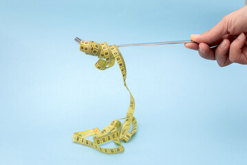 Hand Holding Fork with Flowing Measuring yellow Tape on Light Blue Background