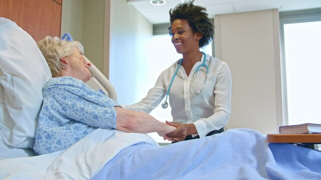 Handheld shot of doctor wearing visiting senior female patient lying in hospital bed giving her good news  - shot in slow motion