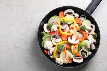 Frying pan with mix of vegetables and mushrooms on light grey table, top view. Space for text