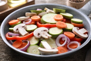Frying pan with mix of fresh vegetables and mushrooms on wooden table, closeup