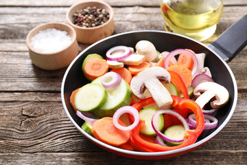 Frying pan with mix of fresh vegetables, mushrooms and spices on wooden table, closeup