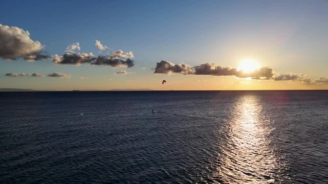  Der Blick zeigt die untergehende Sonne, den Ozean und die Silhouette von Afrika am Horizont. Sanfte Wellen brechen am Ufer, w&auml;hrend der Himmel in warmen Farben leuchtet.
